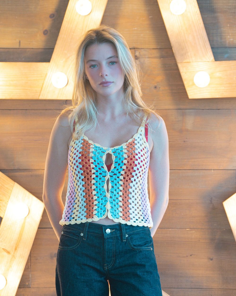 A woman in a striped crochet top and dark jeans stands in front of a lit marquee star.