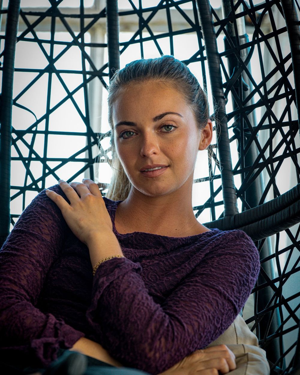 A woman in a plum sweater sits in a black woven hanging chair, one hand on her shoulder.