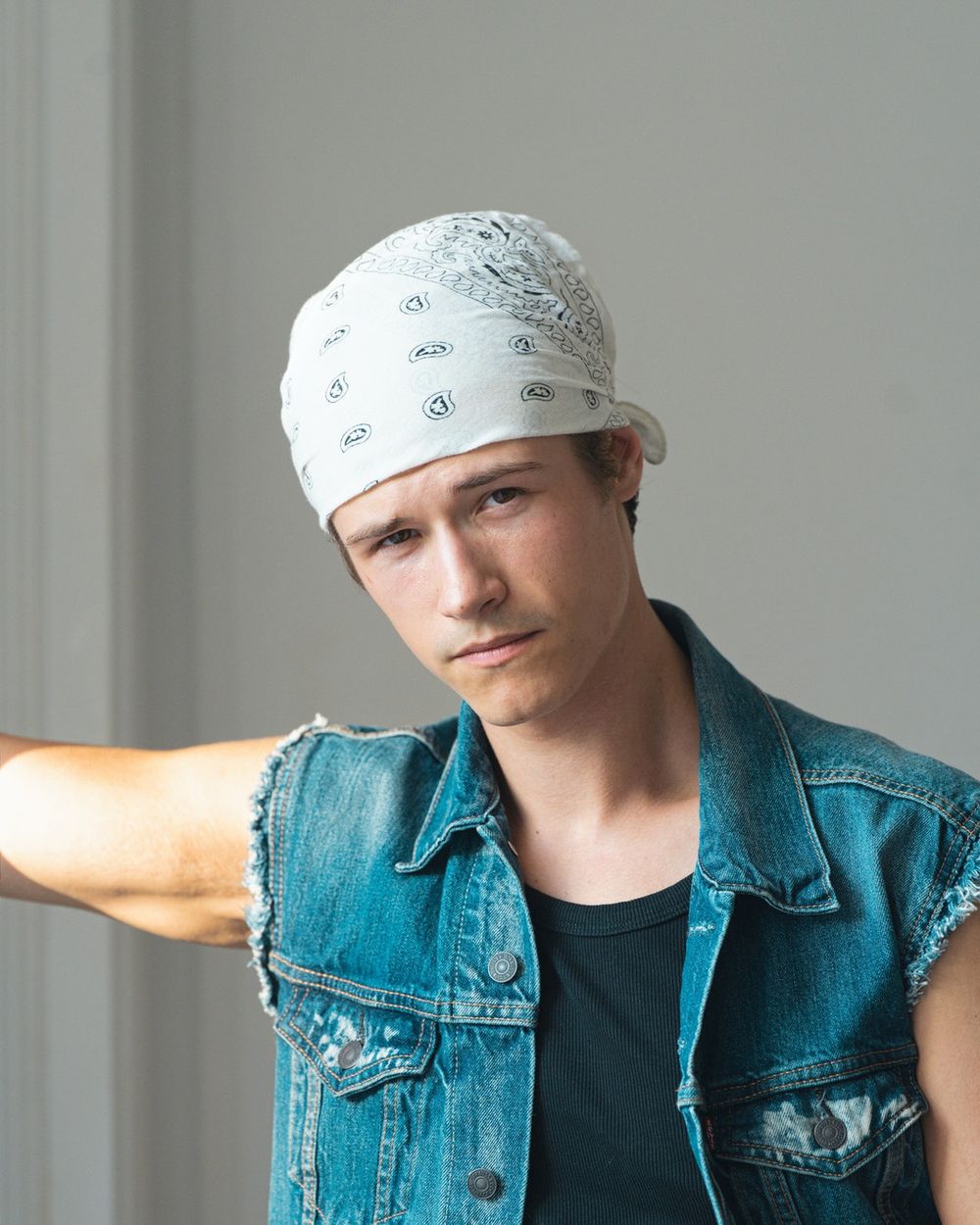 A man in a white bandana and a sleeveless denim vest leans toward the camera.
